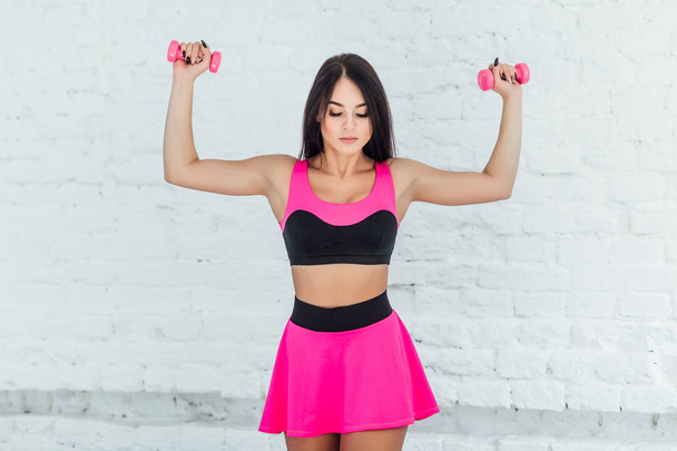 athletic woman with dumbbells pumping up muscles biceps, focus on foreground - Photo, image