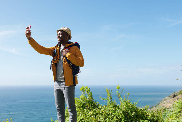 Portrait of happy male traveler taking selfie in nature by sea - Photo, image