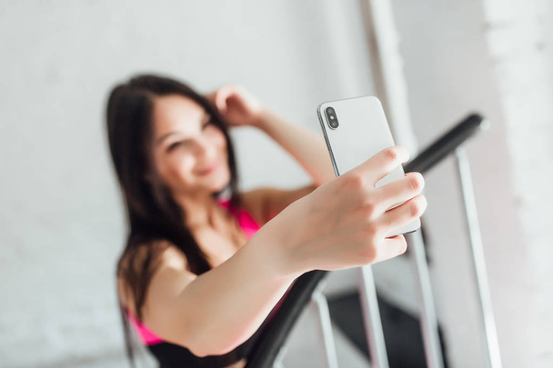 sporty woman holding white smartphone, focus on foreground - Fotó, kép
