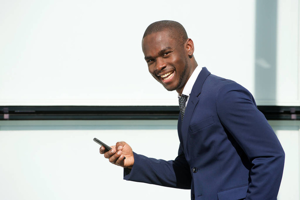 Portrait of happy african businessman walking in city with mobile phone  - Φωτογραφία, εικόνα