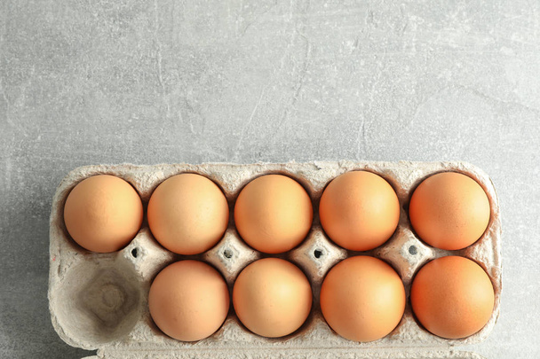 Chicken eggs in carton box on gray background, space for text - Φωτογραφία, εικόνα