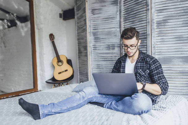 handsome blogger in glasses writing new post for blog for laptop in bed  - Fotó, kép
