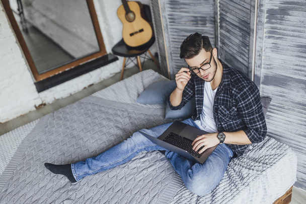handsome man in glasses posing at camera with laptop in hands in studio in loft style - Foto, Imagen