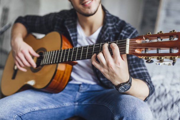 handsome man in glasses smiling and posing with guitar on bed in studio - Foto, Imagen