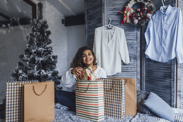 Young beautiful curly blogger unpacking gift bags and in a loft style room - Fotó, kép