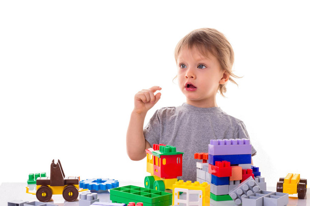 Little boy playing with toy blocks shows a sign of small price with his fingers, surprised face isolated on white background. Toy shop sale and  Early child development concept - Foto, afbeelding