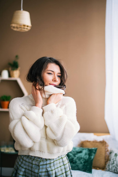 Retrato de bela morena vestida com suéter branco relaxante dentro de casa
 - Foto, Imagem