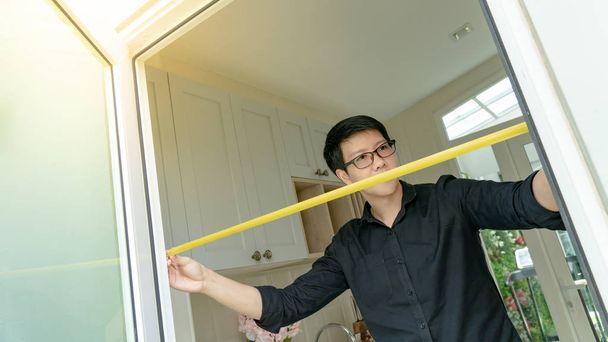 Азиатский мужчина с помощью рулетки на дверной раме
 - Фото, изображение