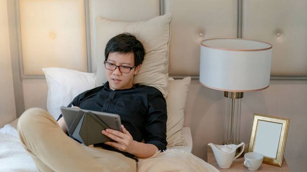 Asian business man using tablet in bedroom - 写真・画像