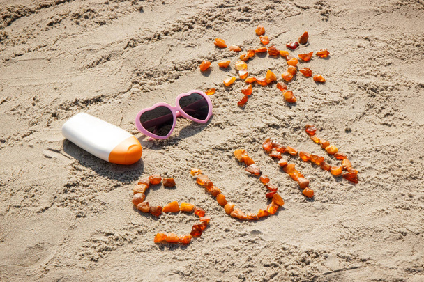 Word and shape of sun, sunglasses with sun lotion on sand at beach, summer time concept - Foto, Imagem