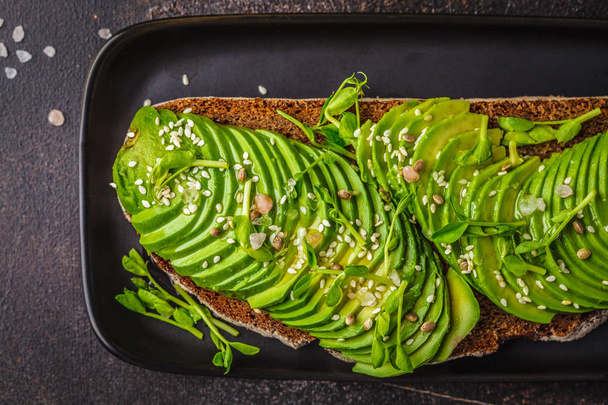 Avocado toast with rye bread and seeds on black plate, dark back - Foto, afbeelding