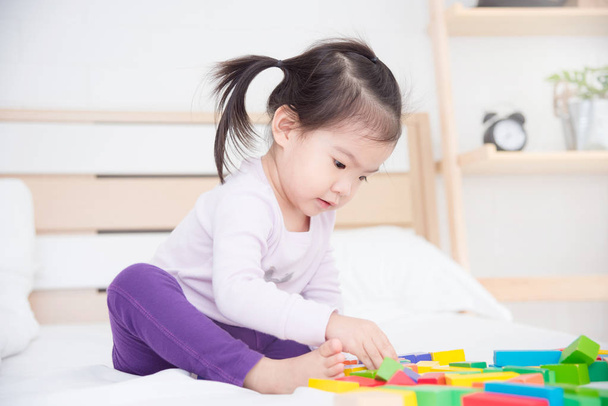 Ázsiai kislány ül ágyas és játék játékok  - Fotó, kép