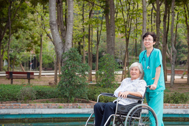 Onnellinen aasialainen vanhempi nainen pyörätuolissa sairaanhoitaja puutarhassa
 - Valokuva, kuva