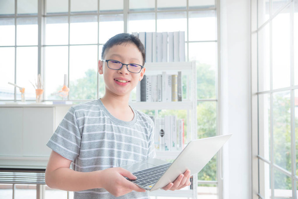 Молодий азіатський хлопчик тримає ноутбук комп'ютера в бібліотеці і посміхається
 - Фото, зображення