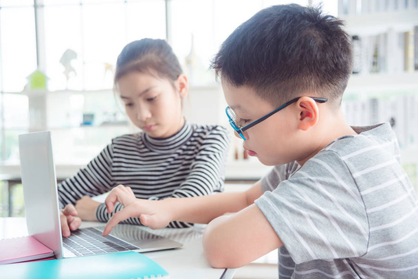 Jeunes enfants asiatiques utilisant un ordinateur portable à la bibliothèque de l'école
 - Photo, image