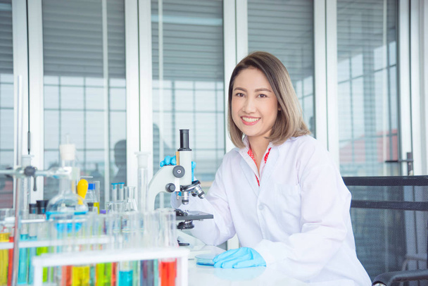 Beautiful scientist in white coat sitting in lab and smile - Photo, Image