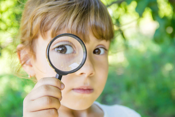 The child is looking in a magnifying glass. Increase. selective focus. - Photo, Image