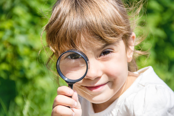 The child is looking in a magnifying glass. Increase. selective focus. - Foto, afbeelding