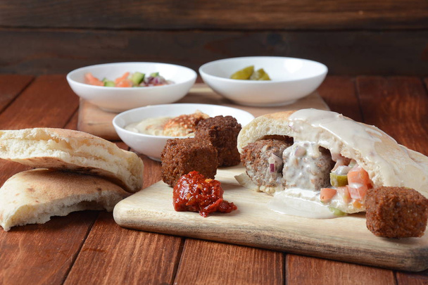 野菜サラダ、ハリッサ ソース、腐植、木製の背景にタヒニ入りピタパンにファラフェル。中東のファーストフードのコンセプト。イスラエルの伝統料理. - 写真・画像