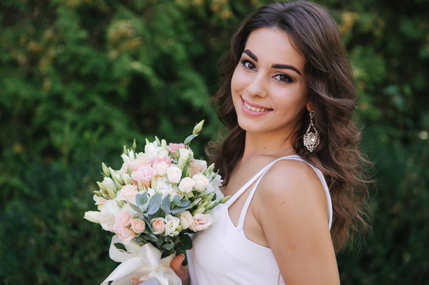 Gorgeous female in white dress slime. Beautiful girl hold a bouquet of flowers in hands - Fotografie, Obrázek