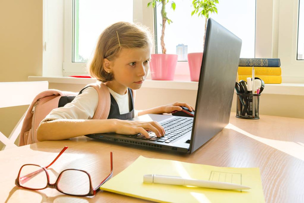La piccola studentessa di 8 anni in uniforme scolastica con uno zaino usa il computer portatile. Scuola, istruzione, conoscenza e bambini
 - Foto, immagini