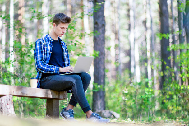 Teenage boy working on a laptop in a green forest park. - Foto, Bild
