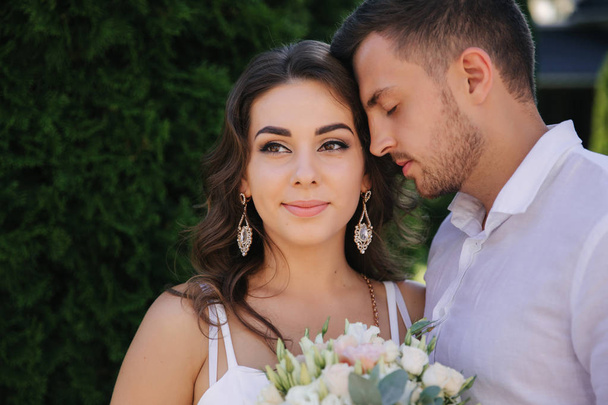 Handsome bearded man kiss his wife. Gogeous woman in white dress with beautiful bouquet. Stylish man in white shirt - Photo, Image