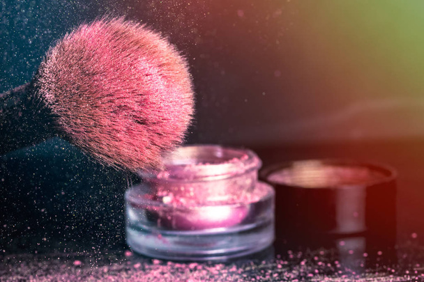 Sombras rosadas, purpurina en el cepillo cosmético y un frasco con tapa sobre fondo oscuro
 - Foto, Imagen