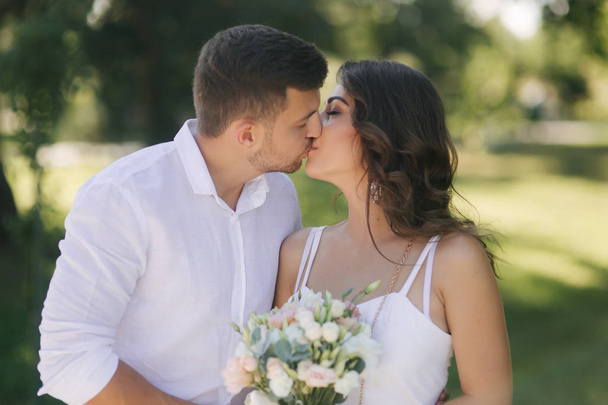 Handsome bearded man kiss his wife. Gogeous woman in white dress with beautiful bouquet. Stylish man in white shirt - Fotoğraf, Görsel