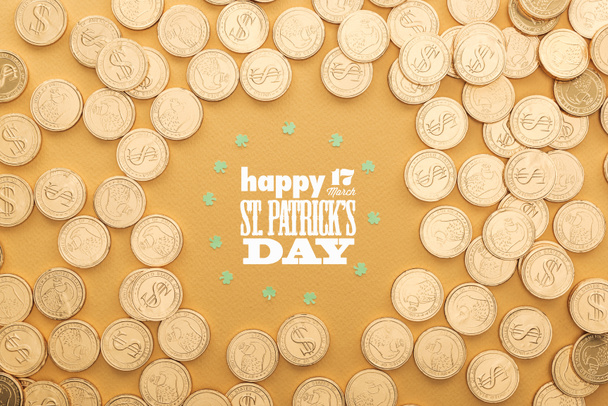 top view of golden coins with dollar signs and circle of shamrocks near happy st patricks day lettering on orange background - Фото, изображение