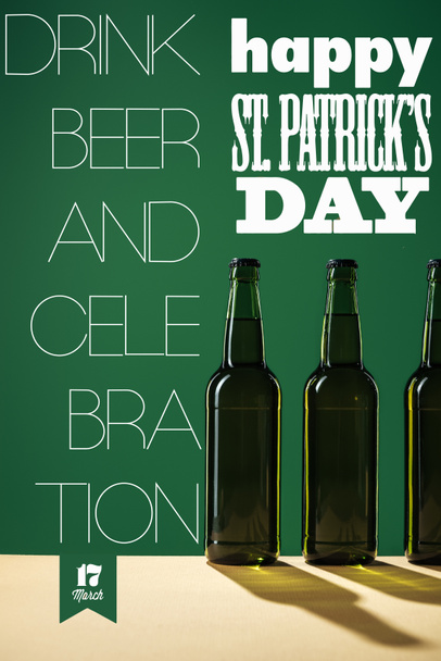 glass beer bottles near happy st patricks day lettering on green background - Фото, изображение