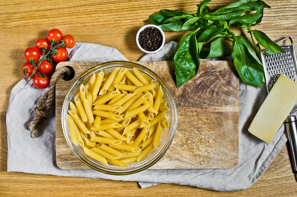 Паста Пенне, ингредиенты для приготовления пищи. Черри помидоры, базилик, пармезан, перец. Деревянный фон, вид сверху
 - Фото, изображение