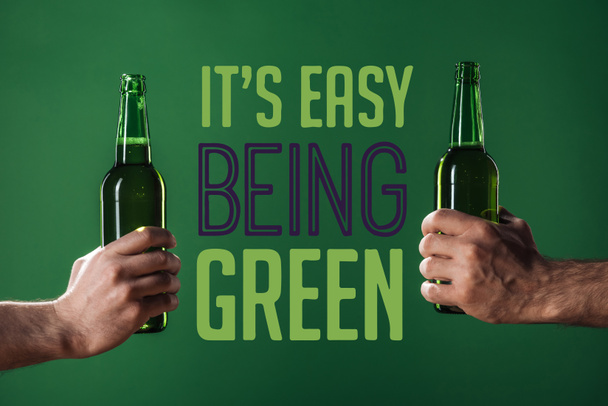 cropped view of men holding beer bottles near its easy being green lettering on green background - Photo, Image