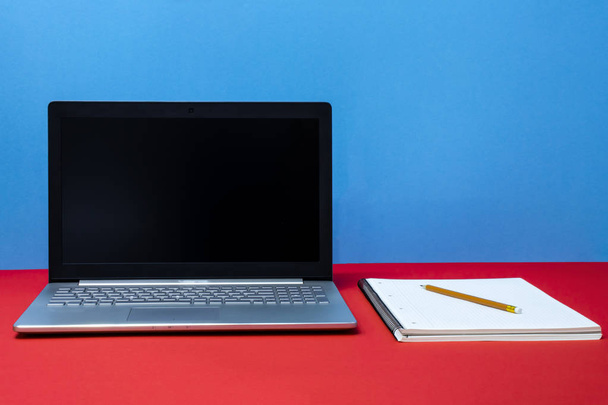 Вид спереду на ноутбук, олівці, блокнот, червоний і синій фон
 - Фото, зображення