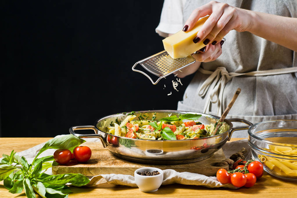シェフは、パスタとフライパンにパルメザン チーズをグリルします。黒の背景、サイドビュー、テキスト用のスペース - 写真・画像