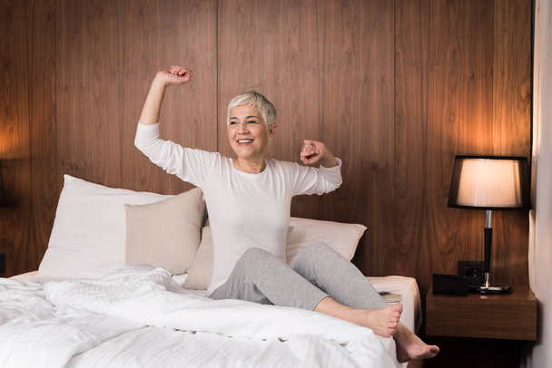 Beautiful senior woman waking up with neck pain and stretching in her bedroom  - Photo, image