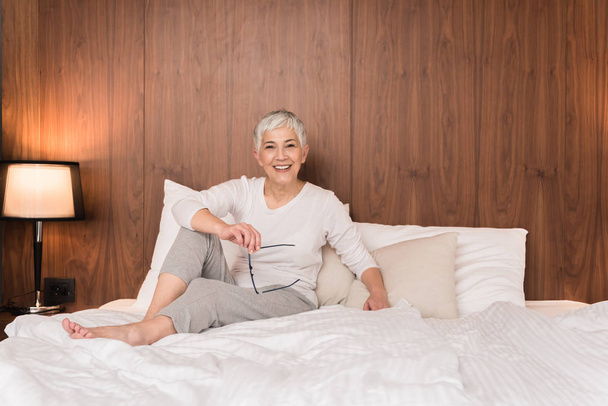 Cheerful senior woman with big beautiful smile sitting on comfy bed  - Photo, image