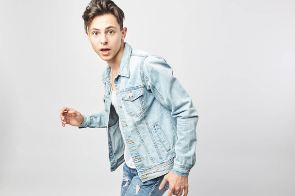 Surprised  guy dark-haired guy dressed in a white t-shirt and a denim jacket stands on the white background in the studio - Photo, Image