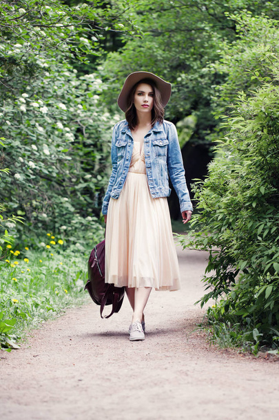 Young woman in denim jacket and hat walking in park outdoors - Photo, Image