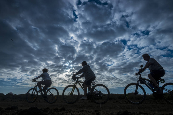 Група людей, які катаються на гірському велосипеді під час красивого темного хмарного заходу сонця
  - Фото, зображення