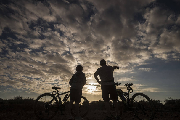 siluety lidí na terénních kolech na pozadí dramatické zamračená obloha - Fotografie, Obrázek