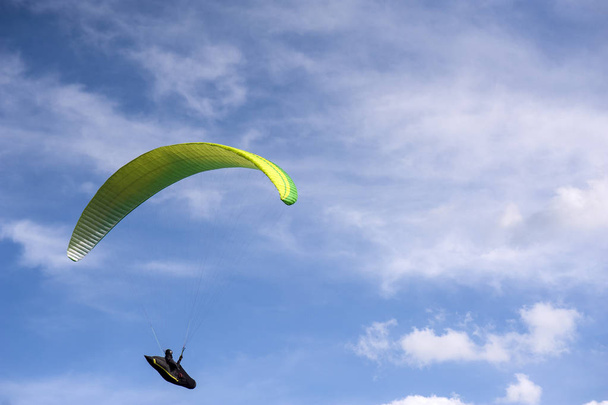 Yellow and green paraglider is flying in the blue sky against th - Photo, Image