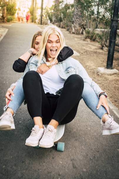 Crazy couple of young woman doing together on the same skate board and having a lot of fun  - Foto, immagini