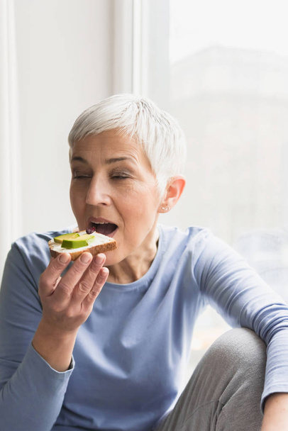 portrait of beautiful mature woman eating healthy nutritious fresh vegan toast with avocado - Фото, изображение