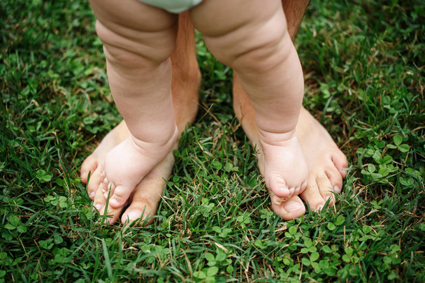 Маленька дитина стоїть на ногах батька на газоні
 - Фото, зображення