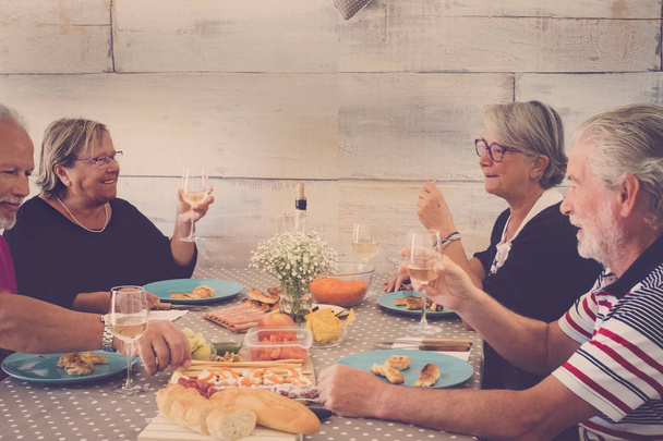 Grupa dorosłych emerytowanych przyjaciół cieszyć się starsze zajęcia rekreacyjne w pomieszczeniach wspólne posiłki w przyjaźni i zabawy ze śmiechem i uśmiechem - szczęśliwy styl życia ludzie koncepcja w domu z jedzeniem i piciem - Zdjęcie, obraz