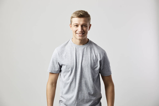Smiling guy dressed in a white t-shirt stands on the white background in the studio - Photo, image