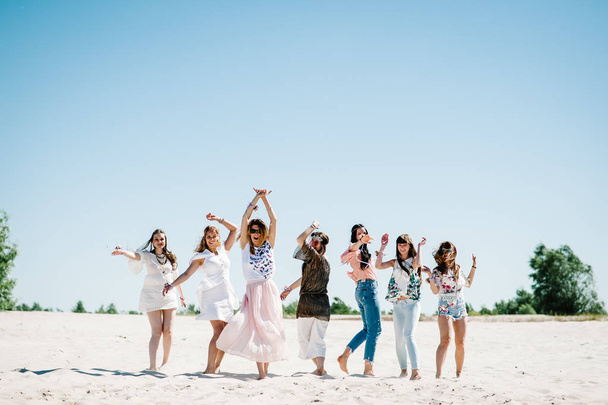 Beautiful stylish happy sexy slim young girls with floral boutonnieres on hands posing on sandy beach. Party in boho style . Maiden evening Hen-parties.  - Foto, imagen