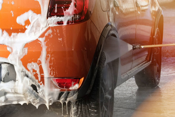 Auto je čištění uvolňován v samoobslužné mytí aut. Bílá pěna na auto. Voda stříkající kolem auta a mýdlová voda stéká. - Fotografie, Obrázek