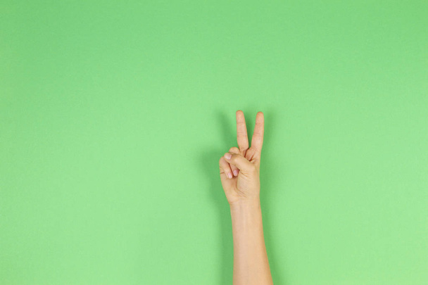 緑の背景を 2 本の指と手を子供します。2 位、勝利または平和のシンボル - 写真・画像